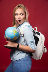 Blonde studentgirl holds a globe and looks surprized
