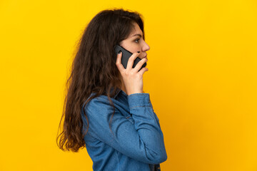 Teenager Russian girl isolated on yellow background keeping a conversation with the mobile phone with someone