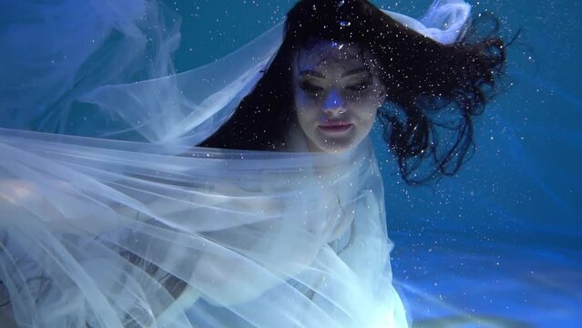 Slow Motion girl in a white dress swims underwater