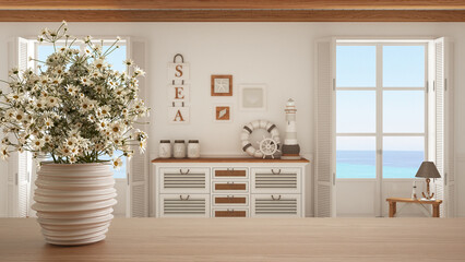 Wooden table top or shelf with pottery vase with daisies, wild flowers, over living room with chest of drawers, marine style, nautical interior design concept