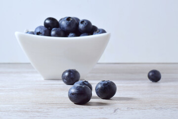 Close up, blueberries in porcelain bowl and scattered on the table.