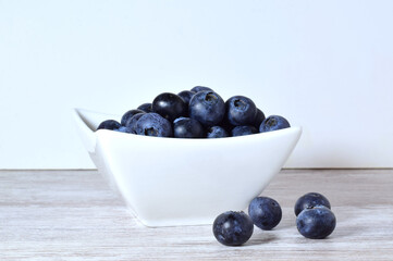 Blueberries in porcelain bowl and scattered on the table.