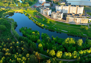 Residential high-rise buildings in the city near river. Townhouses and multi-floor home, aerial view. River in city on sunrise. Multi-storey residential building. City landscape in green background.