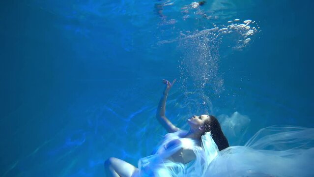 Slow Motion Girl on the ocean floor among the light beams passing through water.