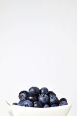 Blueberries in porcelain bowl, light background and copy space.