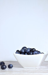 Blueberries in porcelain bowl, light background and copy space.