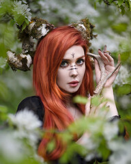 Portrait of a red-haired witch with horns among flowers