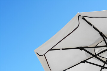 Beautiful white beach umbrella against blue sky. Space for text