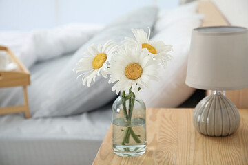 Bouquet of beautiful daisy flowers and lamp on nightstand in bedroom
