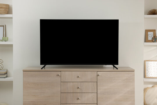 Stylish wide TV set on wooden cabinet in room