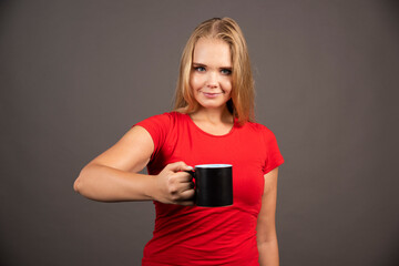 Young woman with empty cup standing on dark background