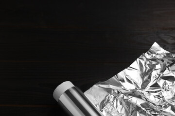 Roll of aluminum foil on dark wooden table, above view. Space for text