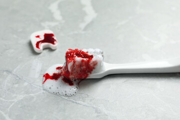 Decorative tooth and toothbrush with blood on light grey marble table, closeup. Gum inflammation