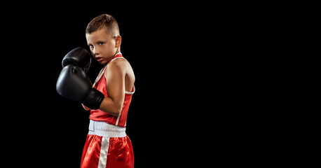 Young beginner boxer, sportive boy training isolated over dark background. Concept of sport,...
