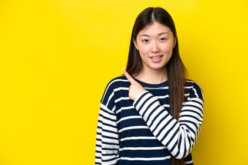 Young Chinese woman isolated on yellow background pointing to the side to present a product