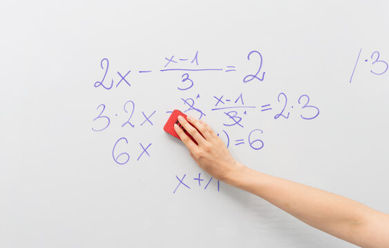 Image of white board  and hand of teacher erasing the math equation from the magnetic white board. Elementary education, math and learning concept.