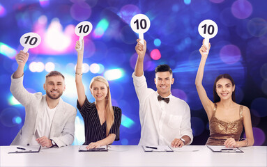Panel of judges holding signs with highest score at table against blurred background. Bokeh effect