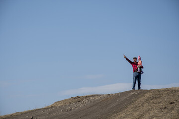 A man in a red plaid shirt stands with a child in his arms, points his finger at the sky