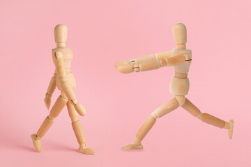 Wooden human models in different poses on pink background