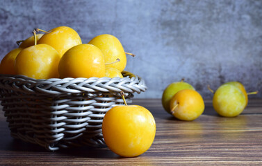 Close up, yellow plum and group on wicker basket. Wooden base stone background. Front shot and copy space.