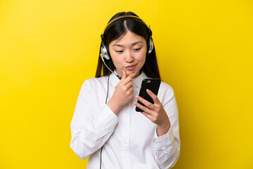 Telemarketer Chinese woman working with a headset isolated on yellow background thinking and sending a message