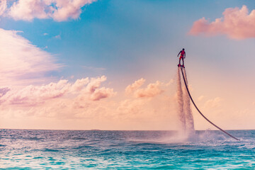 Maldives island sunset. Professional fly board rider doing back flip with tropical resort island...