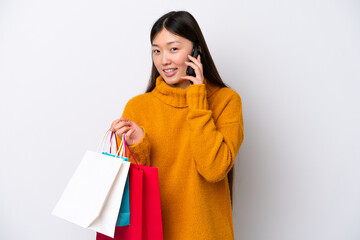 Young Chinese woman isolated on white background holding shopping bags and calling a friend with her cell phone