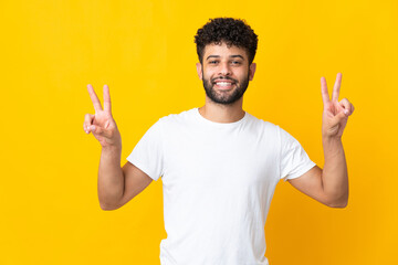 Young Moroccan man isolated on yellow background showing victory sign with both hands