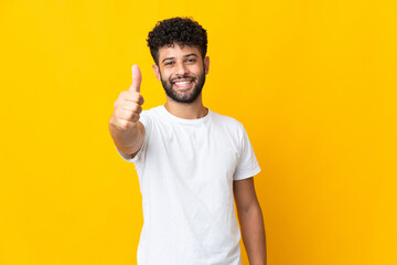 Young Moroccan man isolated on yellow background with thumbs up because something good has happened