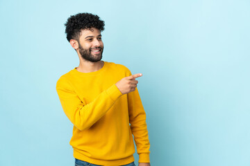 Young Moroccan man isolated on blue background pointing finger to the side and presenting a product