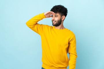 Young Moroccan man isolated on blue background with surprise expression while looking side