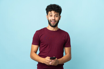 Young Moroccan man isolated on blue background surprised and sending a message