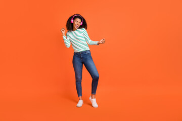 Full body photo of young lady dance wear headphones shirt jeans sneakers isolated on orange background