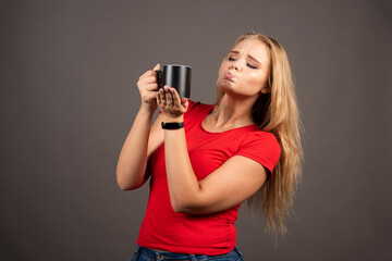 Young woman making face at empty cup on dark background