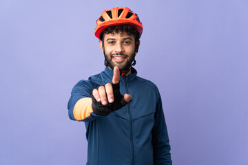 Young Moroccan cyclist man isolated on purple background showing and lifting a finger