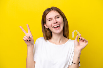 Young English woman holding invisible braces smiling and showing victory sign