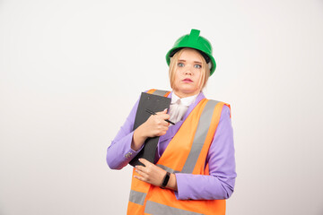 Young female contractor with green helmet and clipboard on white background
