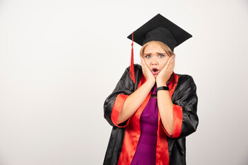 Female student in gown holding her face on white background
