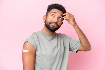 Young Brazilian man wearing a band aid isolated on pink background having doubts and with confuse face expression