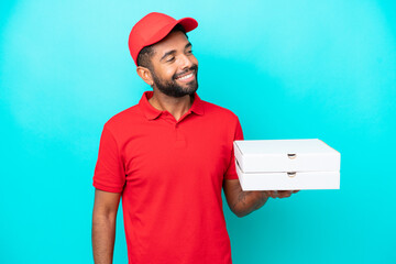 Pizza delivery Brazilian man with work uniform picking up pizza boxes isolated on blue background...