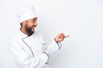 Young Brazilian chef man isolated on white background pointing finger to the side and presenting a...