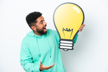 Young Brazilian man isolated on white background holding a bulb icon with surprised expression