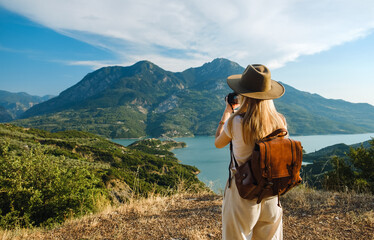 Woman photographer with big backpack taking photo of mountains and blue lake. Travel and hobby...