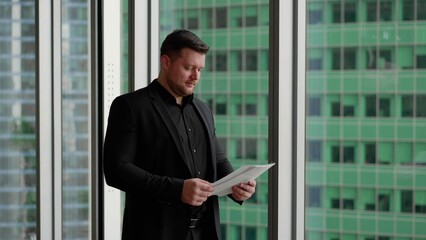 Businessman signs a document on the background of skyscrapers. A man holds documents in his hand and puts his signature on the background of a skyscraper. A businessman signs a document