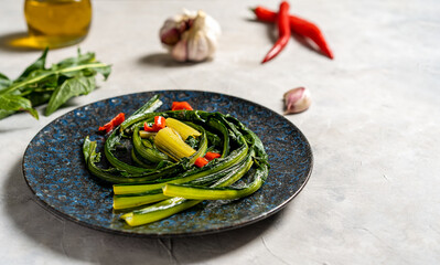 Chicory greens stewed with garlic and hot red paper on blue plate with ingredients aside. Copy space