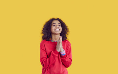 Smiling teen African American girl isolated on yellow studio background keep hands in prayer....