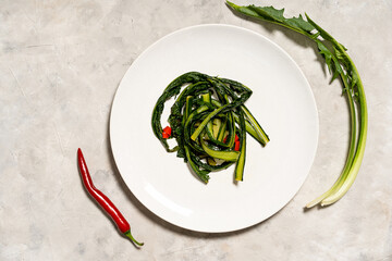 Chicory greens stewed with garlic and hot red paper on plate with ingredients. Top view with copy...