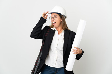 Middle age architect woman with helmet and holding blueprints over isolated background doing surprise gesture while looking to the side