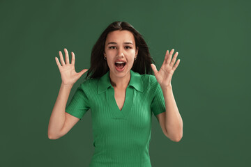 Portrait of emotive young girl posing, showing shocked face isolated over green studio background