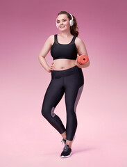 Attractive woman holds yoga or fitness mat after working out. Photo of pretty model with curvy figure in black sportswear on pink background. Sports motivation and healthy lifestyle